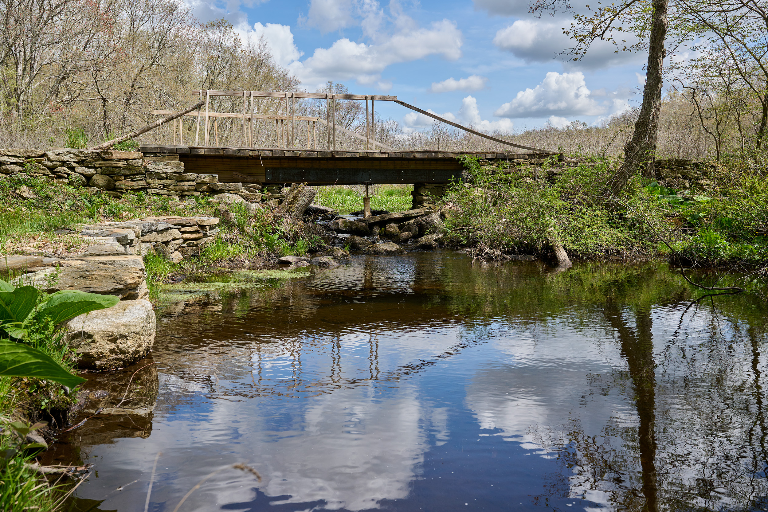 a wooden bridge over a brook that reflects the sky