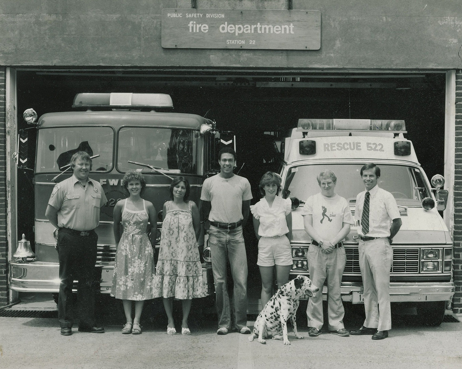 July 14 1982, Cpt. R. Palmer, Mollie Robinson, Norah Harmon, Bob Hopson, Priscilla White, Kraig Bailey, D.P. Bliss, and Freckles pose in front of the fire department building