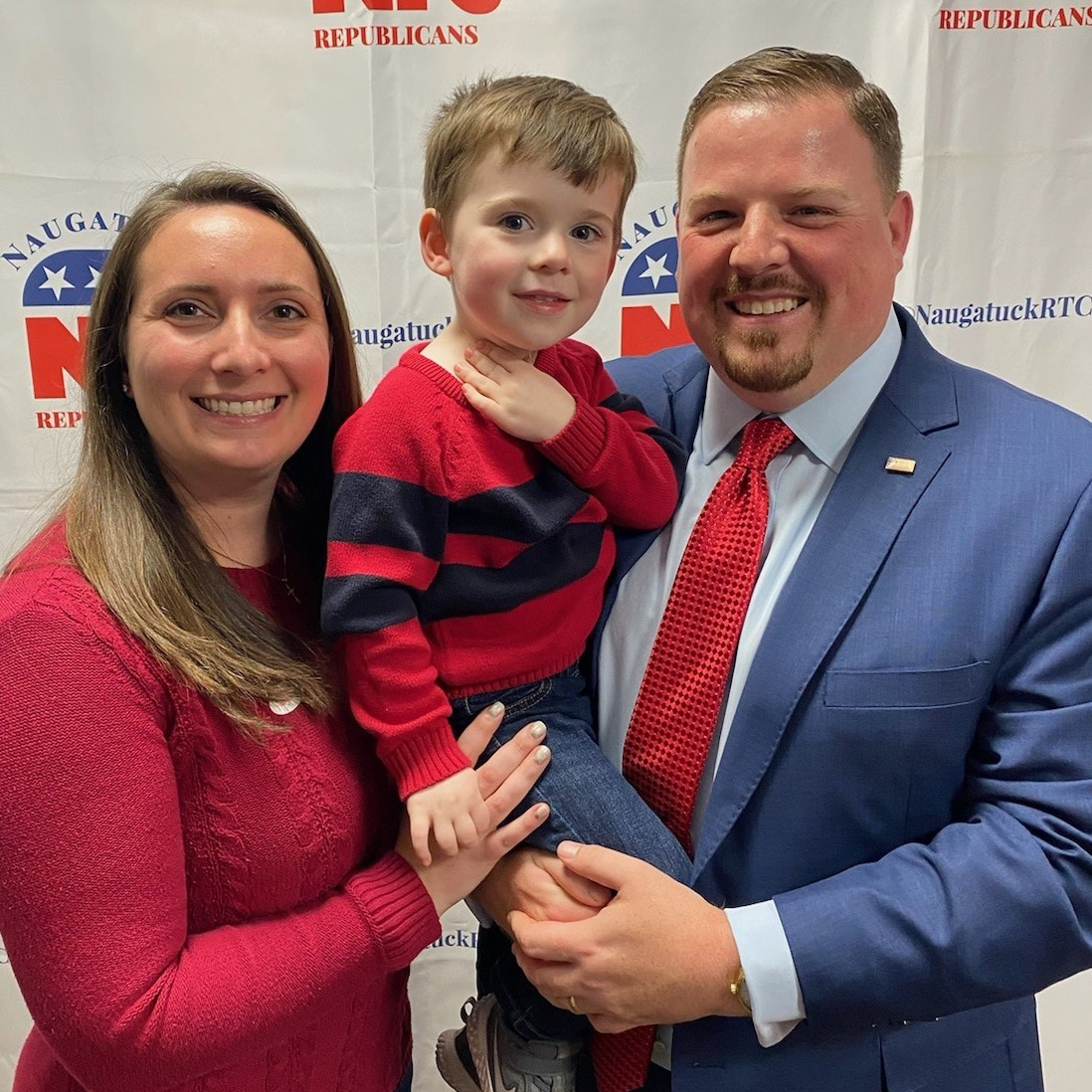 Seth Bronko '11 elected as state rep stands in front of republican banner with wife and child