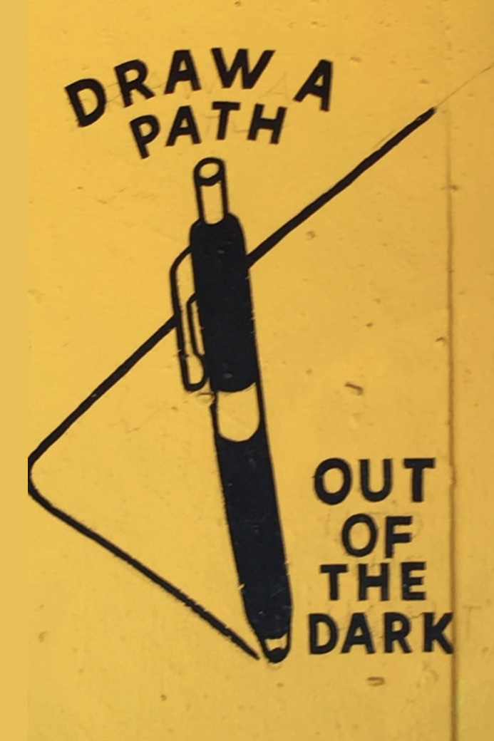 art on a yellow wall depicting a pen painting a path. It reads Draw a path out of the dark.
