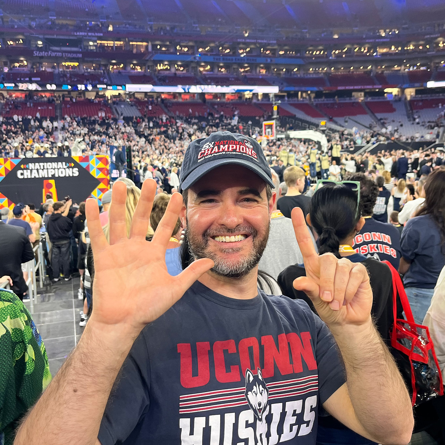 man smiles and holds up 6 fingers representing 6 wins for camera during 2024 UConn men's title game.