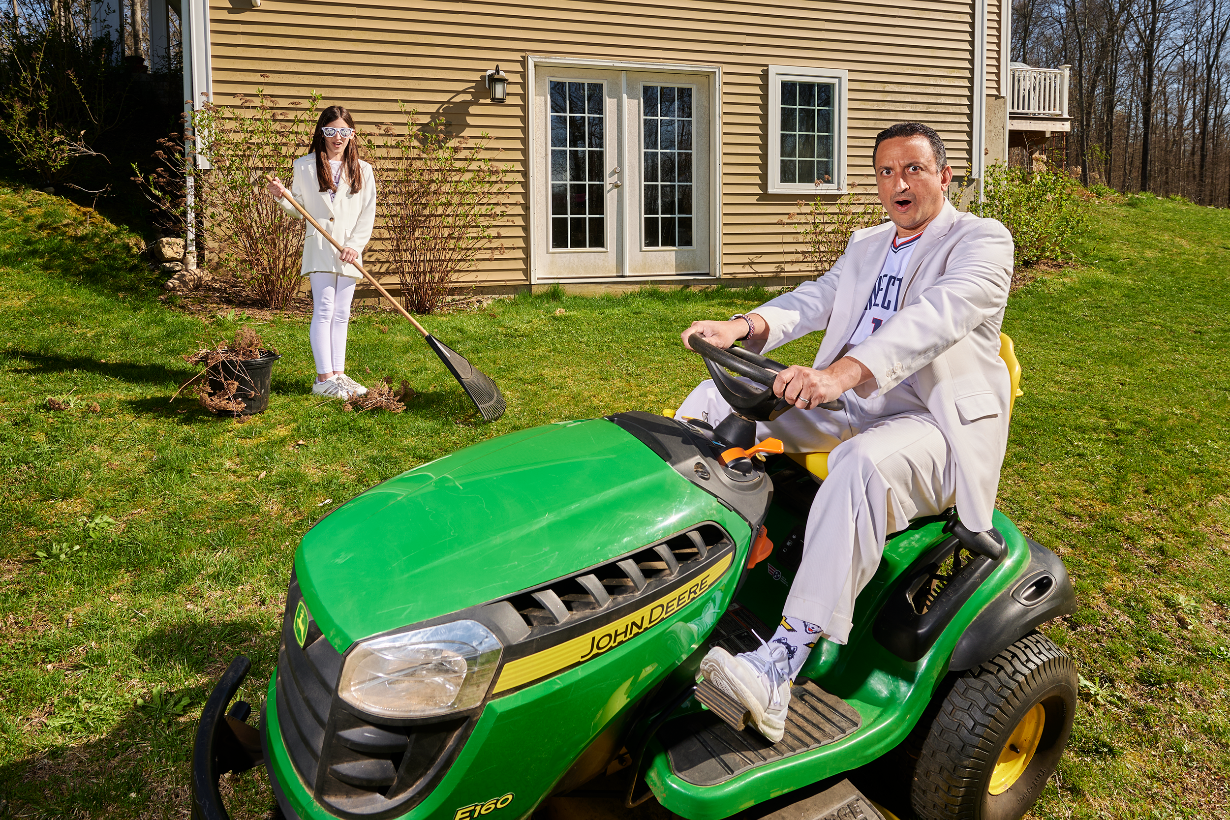 Prem Aithal and his daughter mow and rake their yard in white and blue UConn-branded outfits.