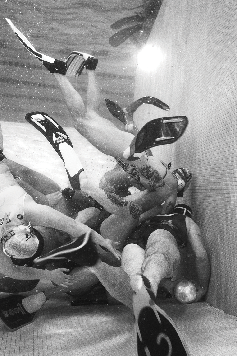 Several Rugby players dive towards a ball underwater in a pool