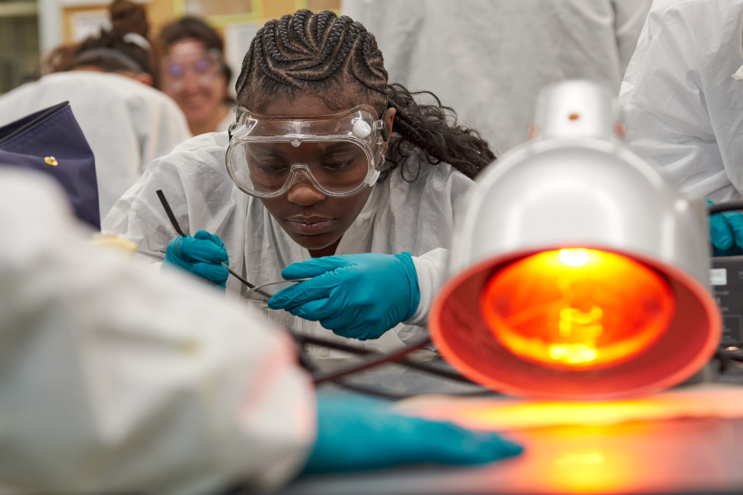 A female student closely examines a slide in a chem lab, while an orange lamp shines on the right.