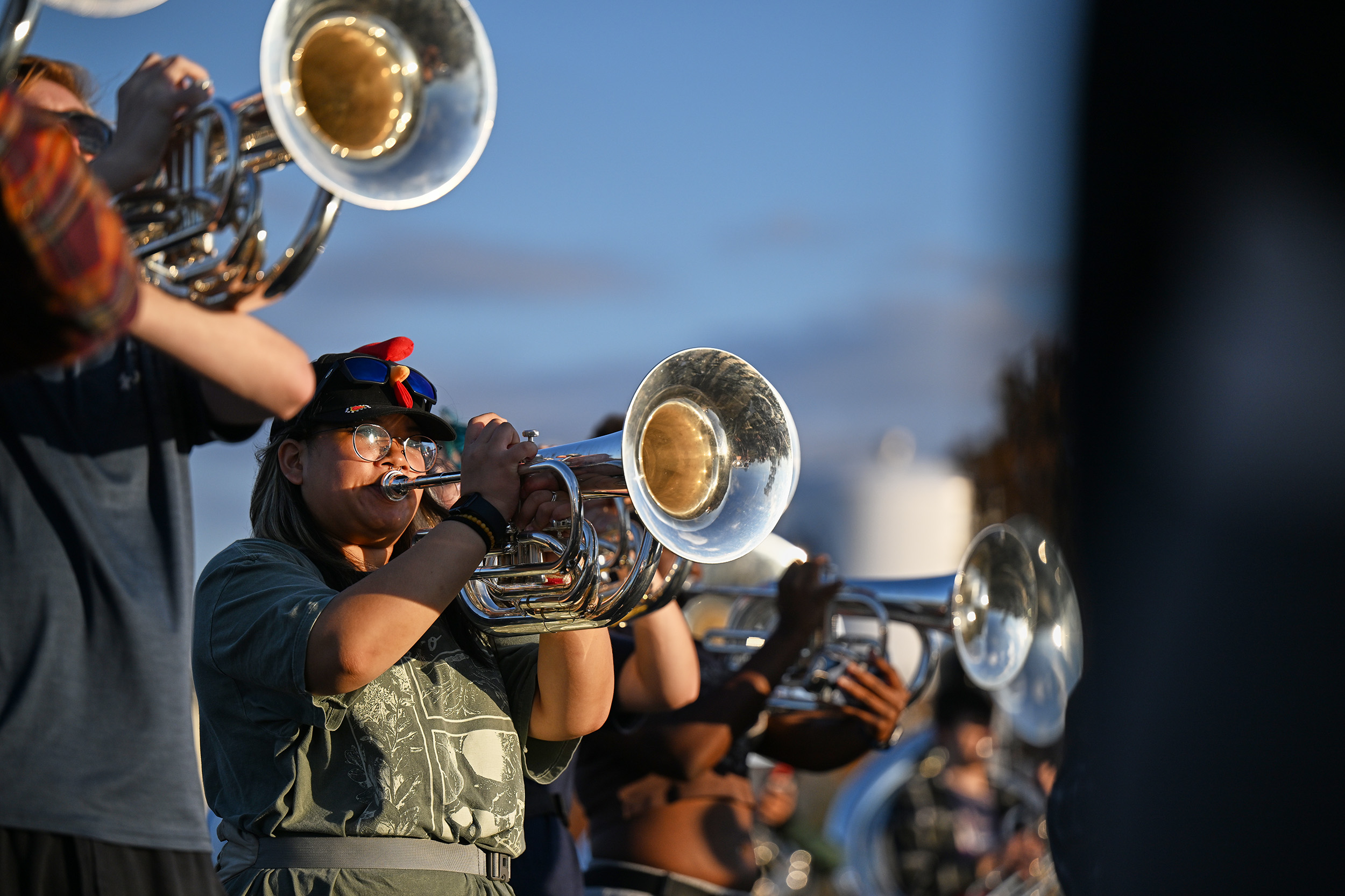 Lineup of students playing the trumpets, the one in the middle wears a rooster hat.