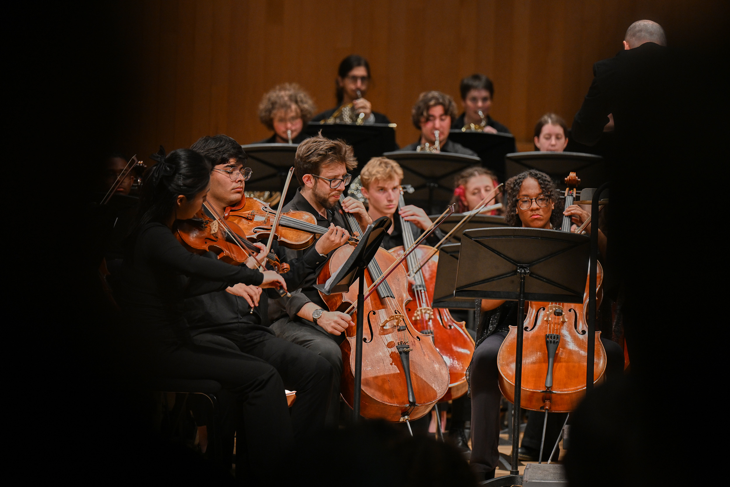 Students perform at the symphony, playing instruments such as bass, violins, and trumpets.