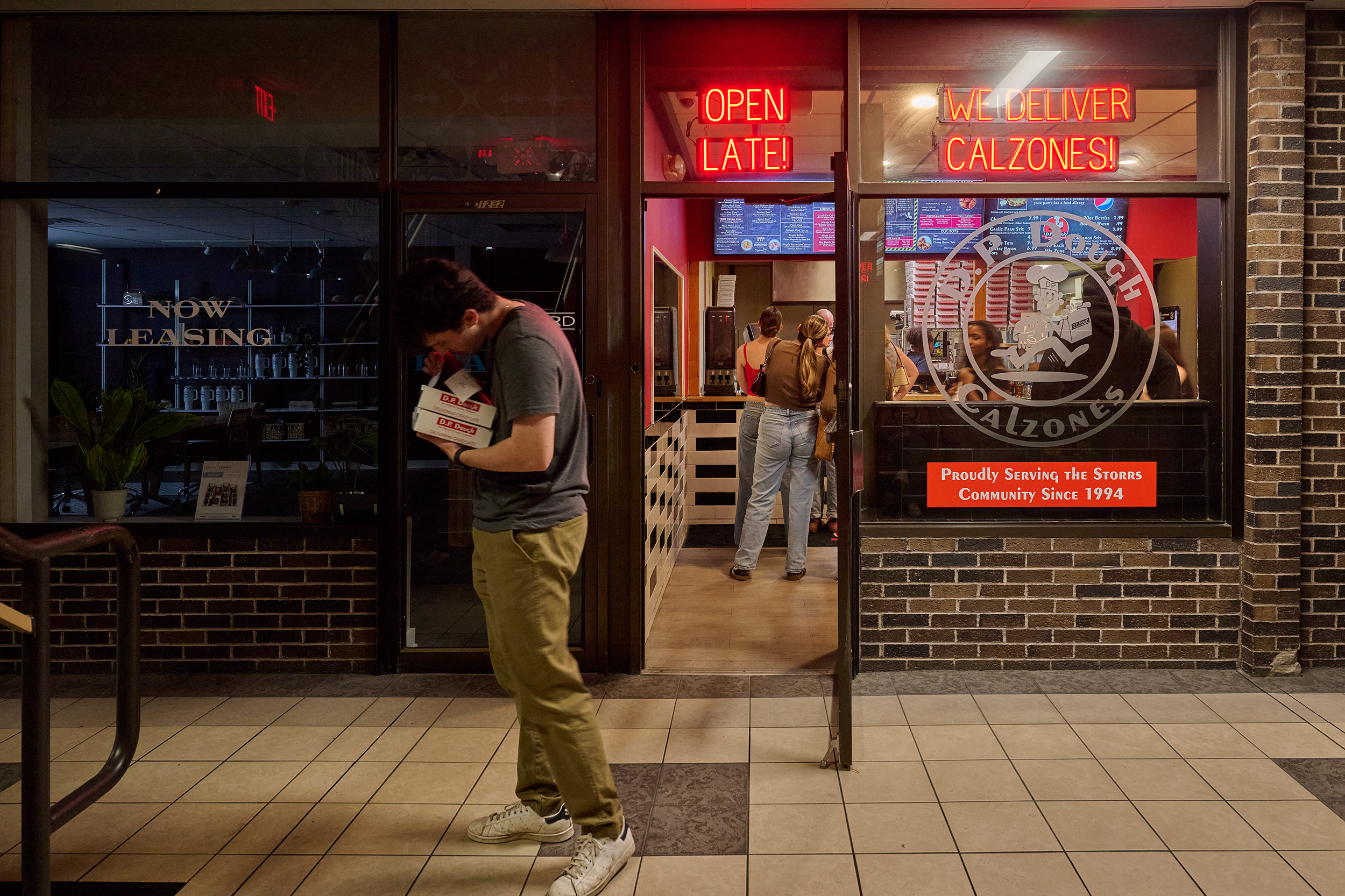 Male student eagerly peeks into his D.P. Dough order, while the shop remains full of students waiting to order.