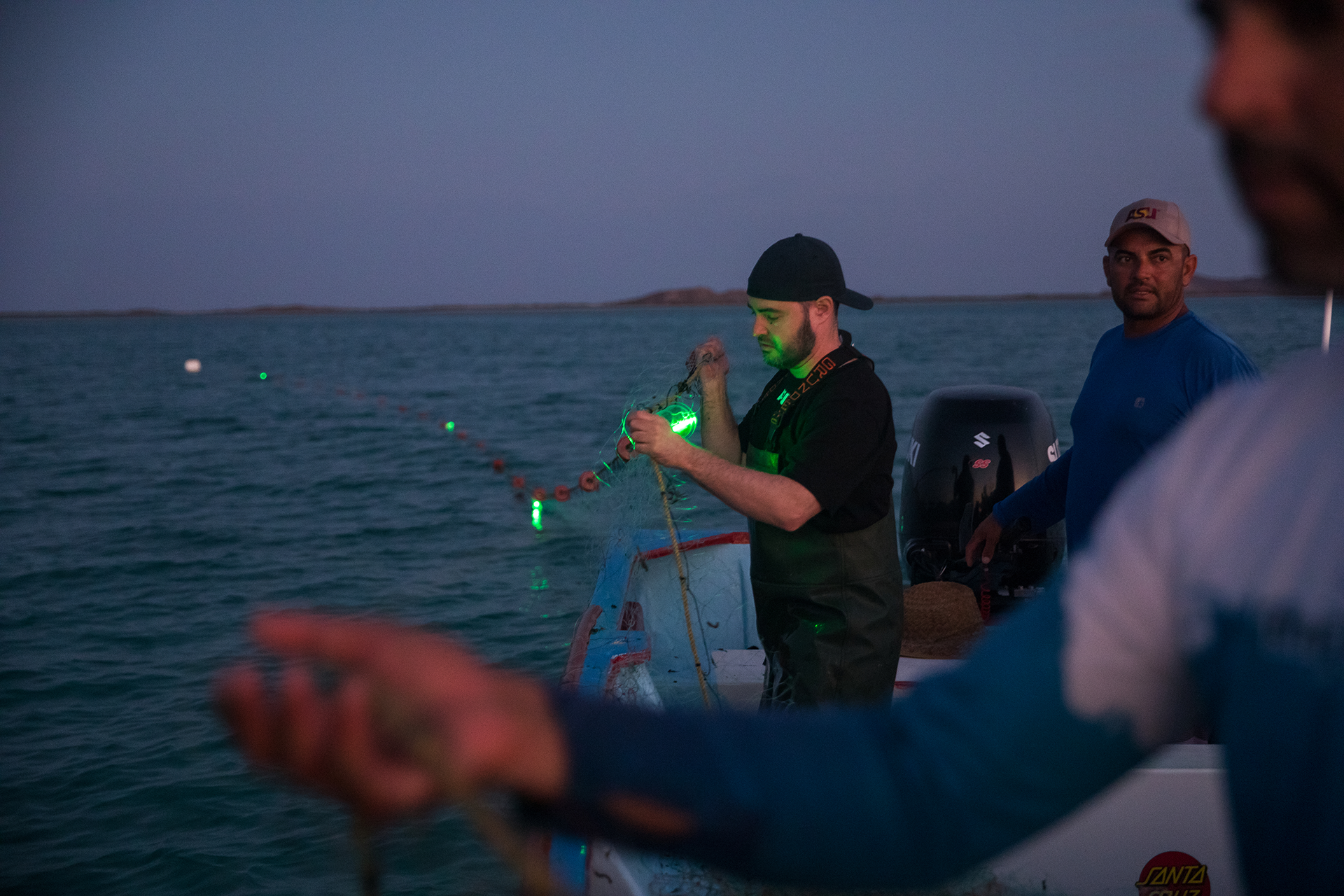 Jesse Senko and fisherman lay out fishing net to test. The net is equipped with lights meant to deter turtles from getting caught