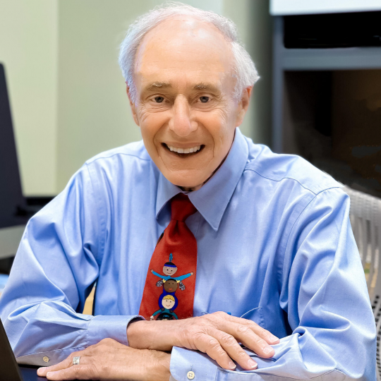Frank Baskind in blue shirt and red tie sitting at a computer
