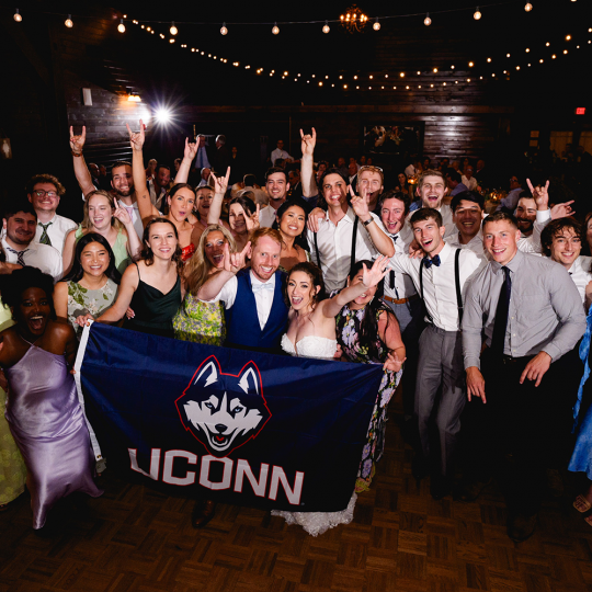 Large group of alums stand with UConn flag at Marissa Gelfand and David Angelo’s wedding