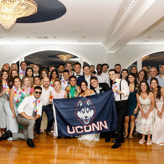 Large group of alums stand with UConn flag at Olivia Levine and Justin Szeglin’s wedding