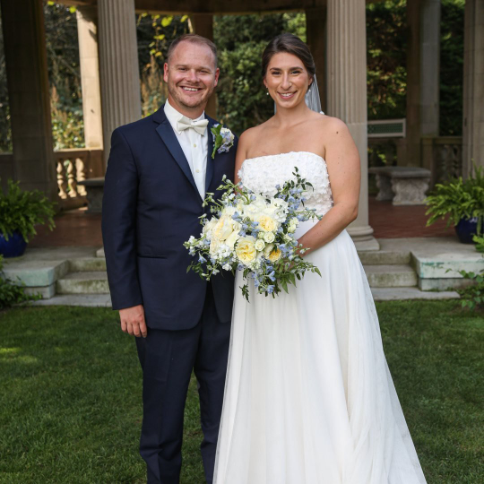 Jeremy Crouse stands in suit next to Rachael Orbe in wedding dress holding wedding bouquet.