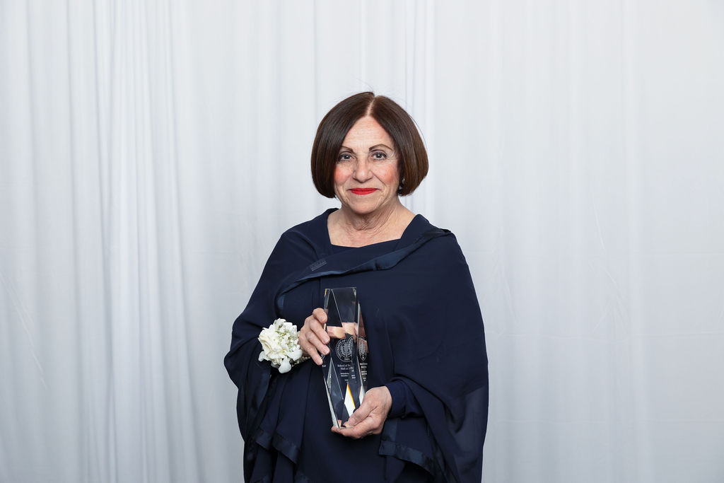 UCONN2024HallofFame-49 Toni Boucher in blue dress holding School of Business Hall of Fame award in front of a grey background