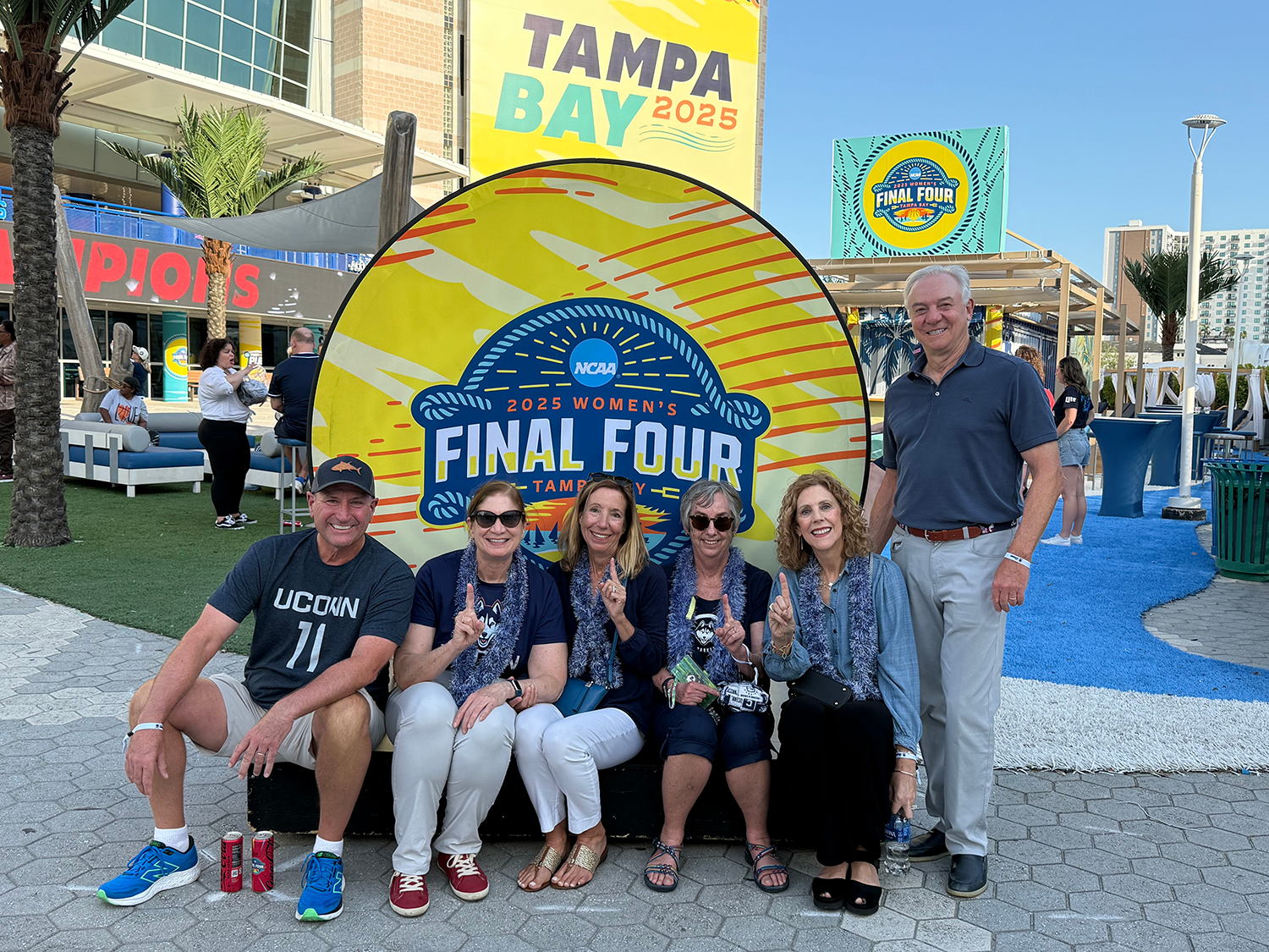 Unknown Group of 6 UConn alums sitting in front of Final Four sign in Tampa Bay for March Madness 2025