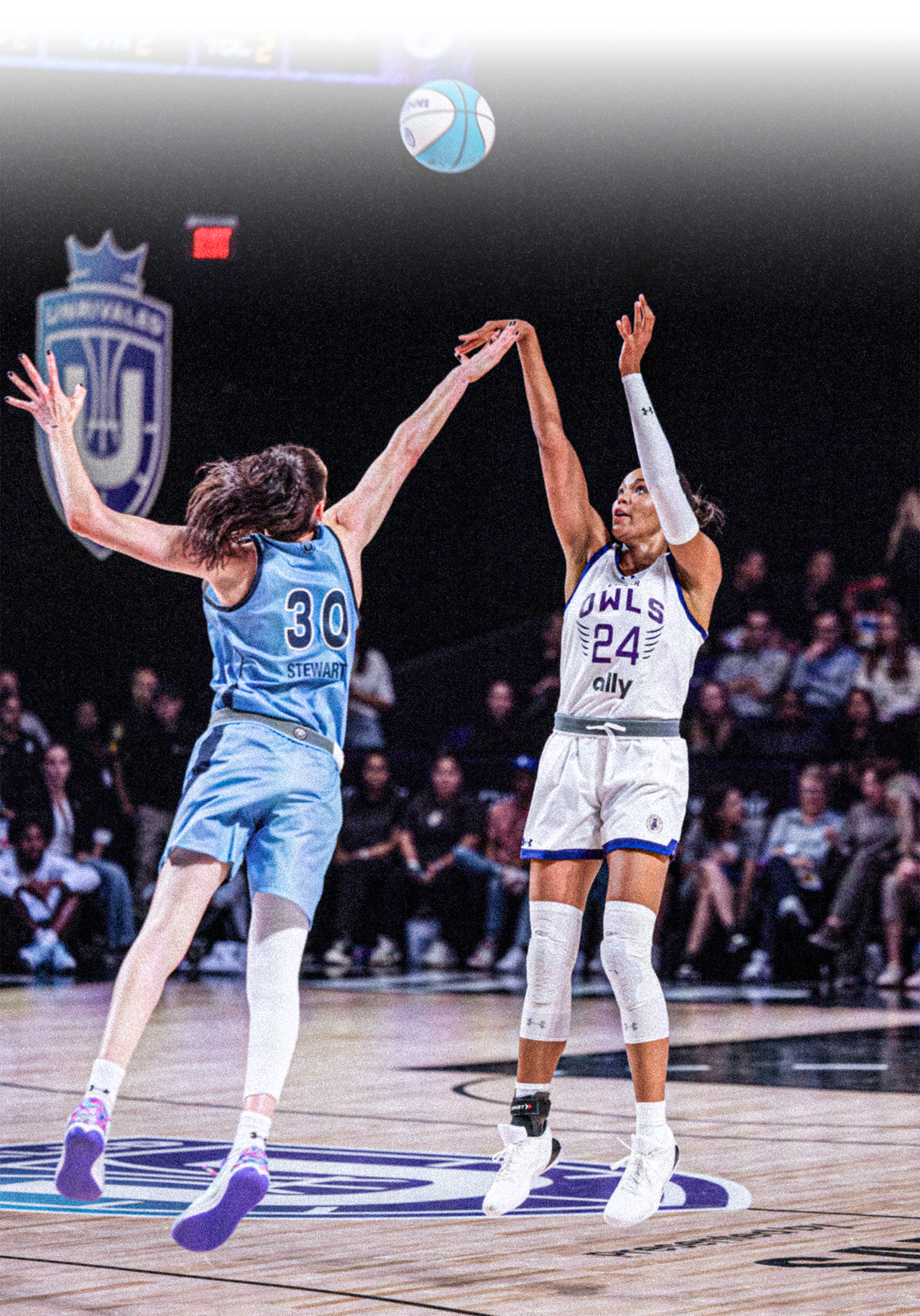 Two female basketball players, one wearing a light blue uniform with number 30 who has her back to the camera and one with a white uniform that reads Owls #24, raise their hands to get the ball during tipoff while a crowd looks on.