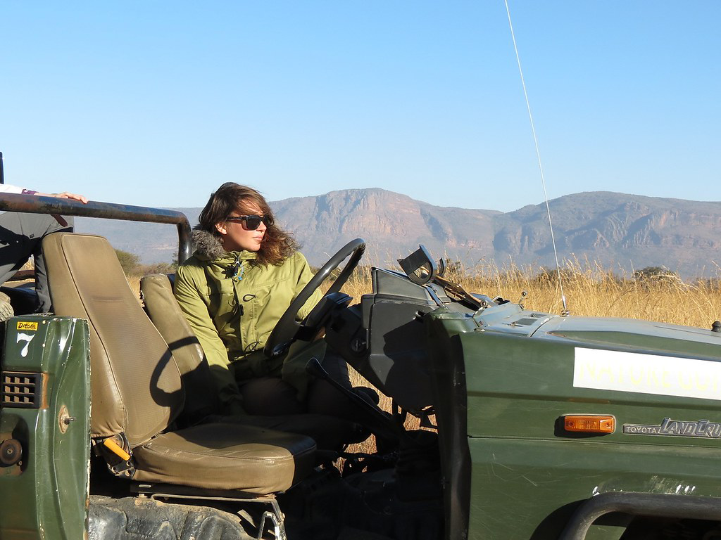 Carly Congdon wears a light green puffy coat with a fur-lined hood in the passenger seat of a dark green open-top Jeep at the Entabeni Game Reserve in South Africa