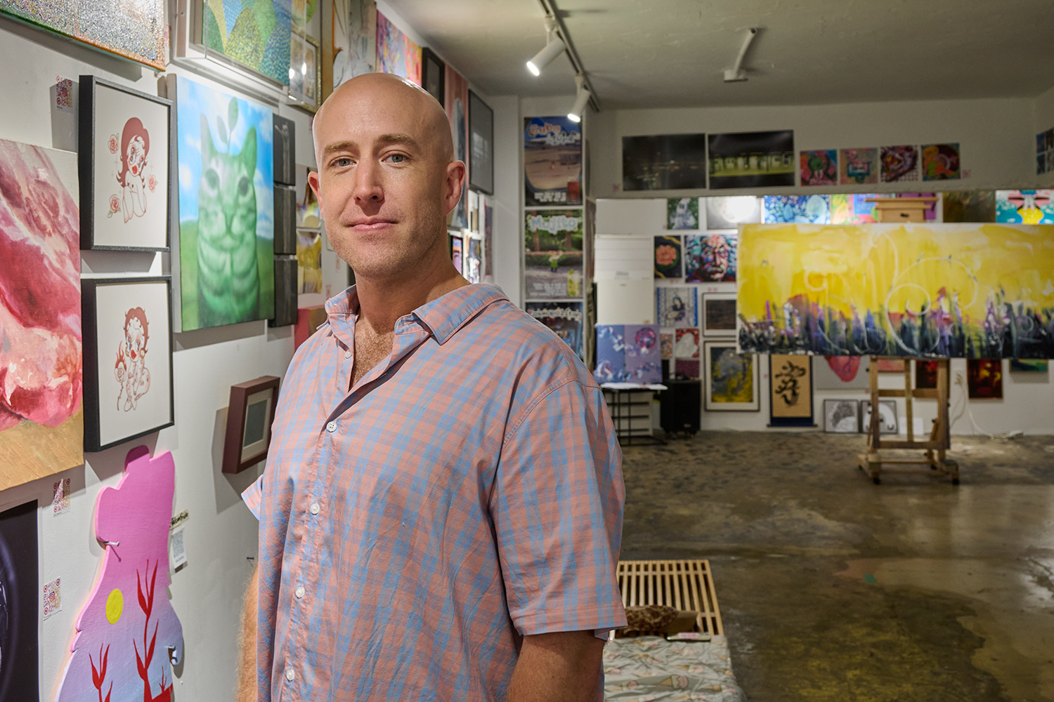 Neil Wheelock Deforest Smith in a gallery with paintings in different colors and styles covering most of the wall space and a large painting on an easel behind him.