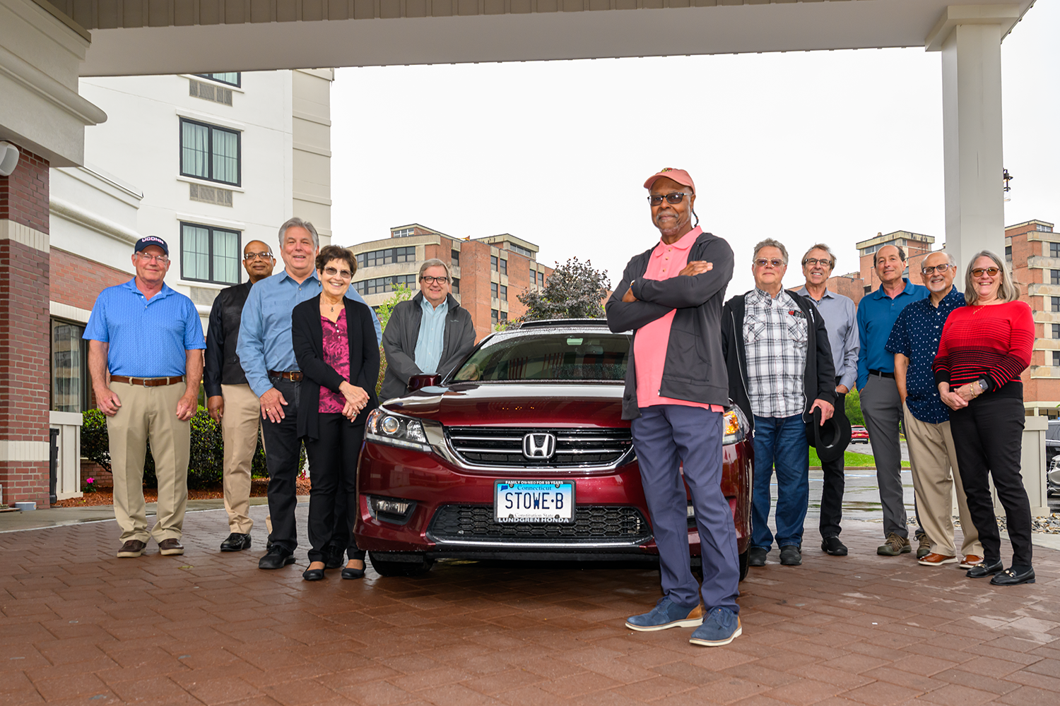the group poses with a red sedan with the license plate that reads, STOWE-B