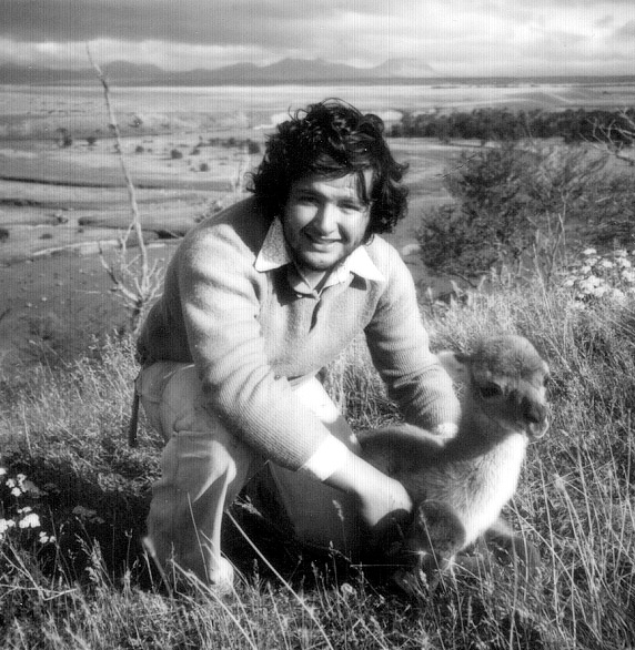 A 20-year-old Morty Ortega crouches down to hold a baby guanaco in a grassy field in Chile in 1976