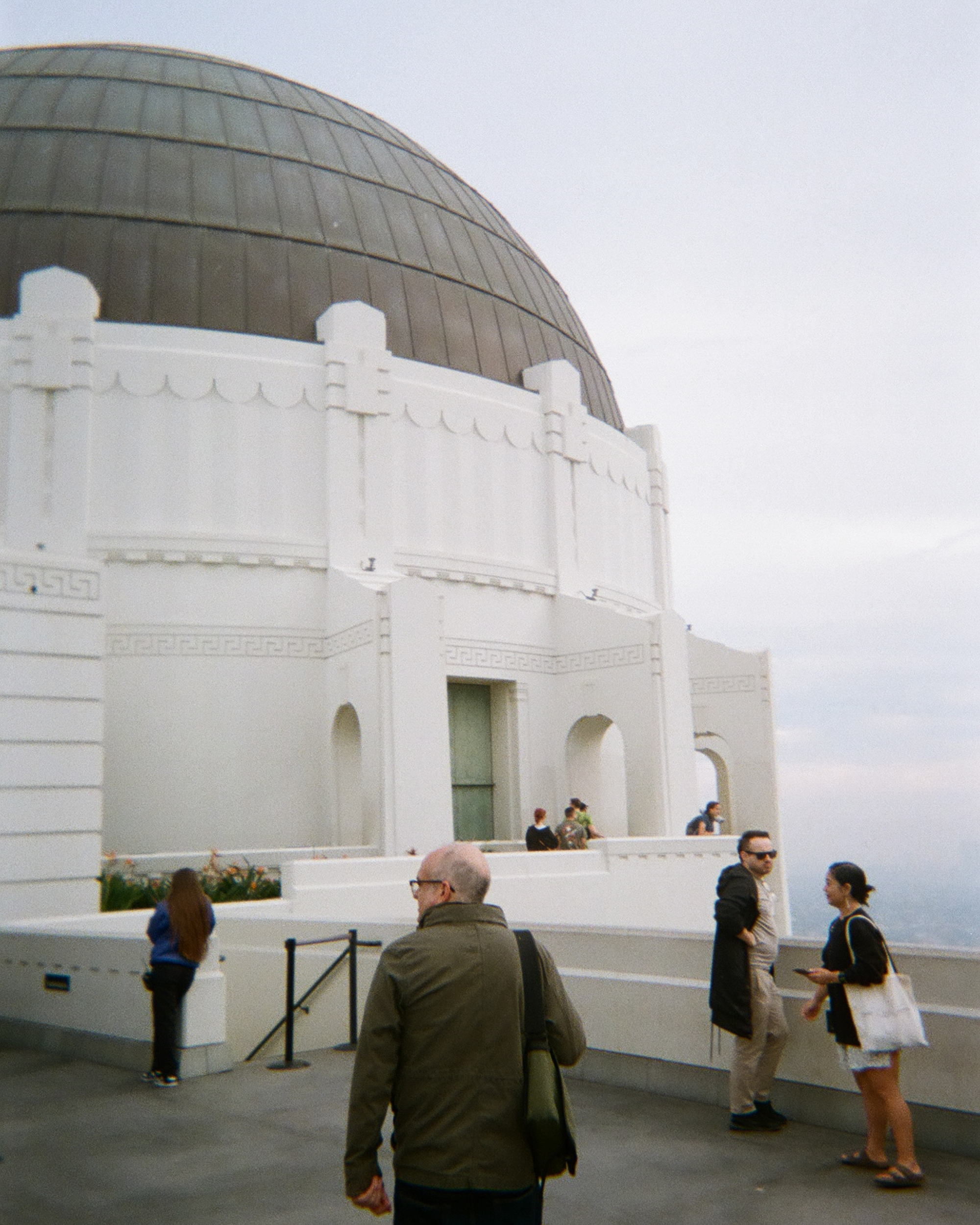 Will Hines in green jacket and tote bag, walks center-frame