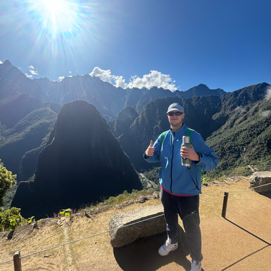 Anduei Xhelaj in Peru, gives a thumbs up as they pose in front of a beautiful overlook.