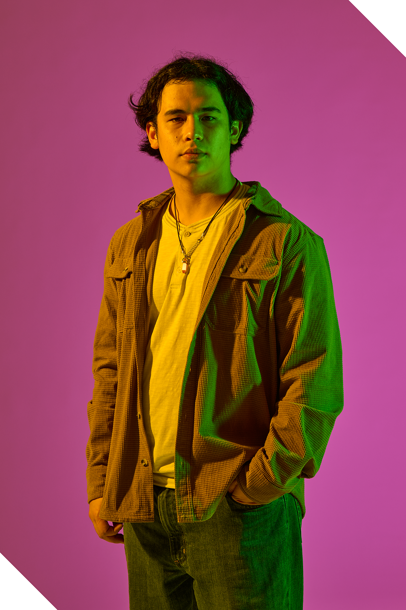 Brendan Toon poses in front of a fuchsia backdrop, highlighted by green and yellow light.