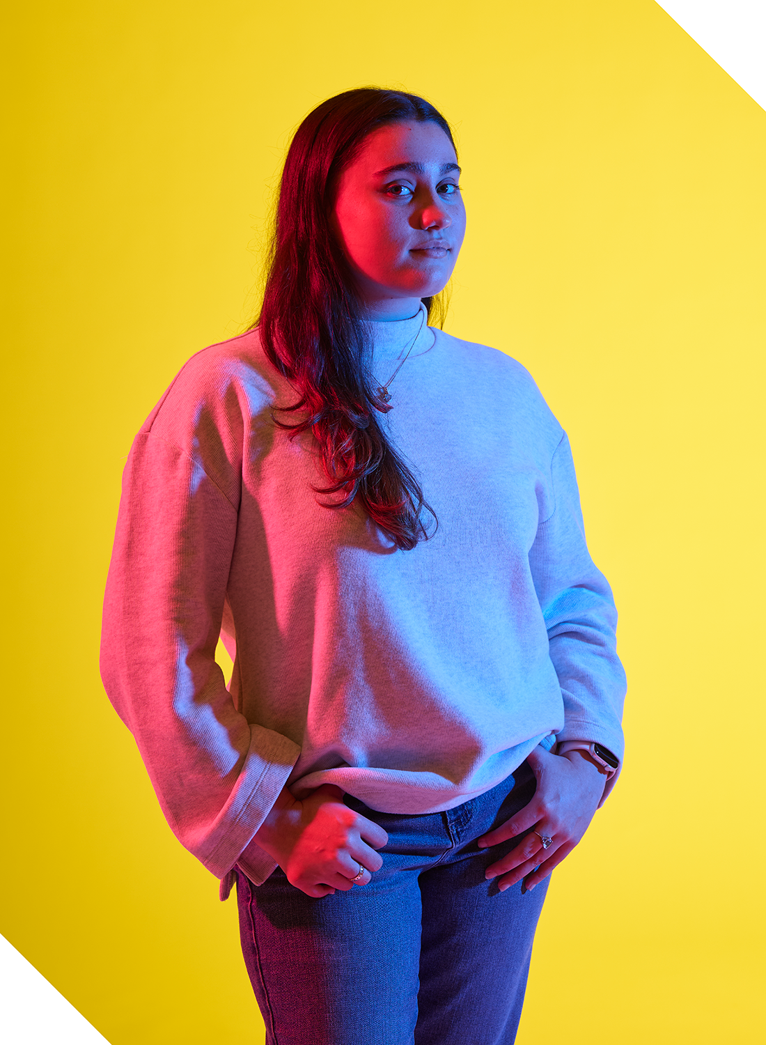 Kiley Girard poses in front of yellow backdrop, with blue and pink lighting.