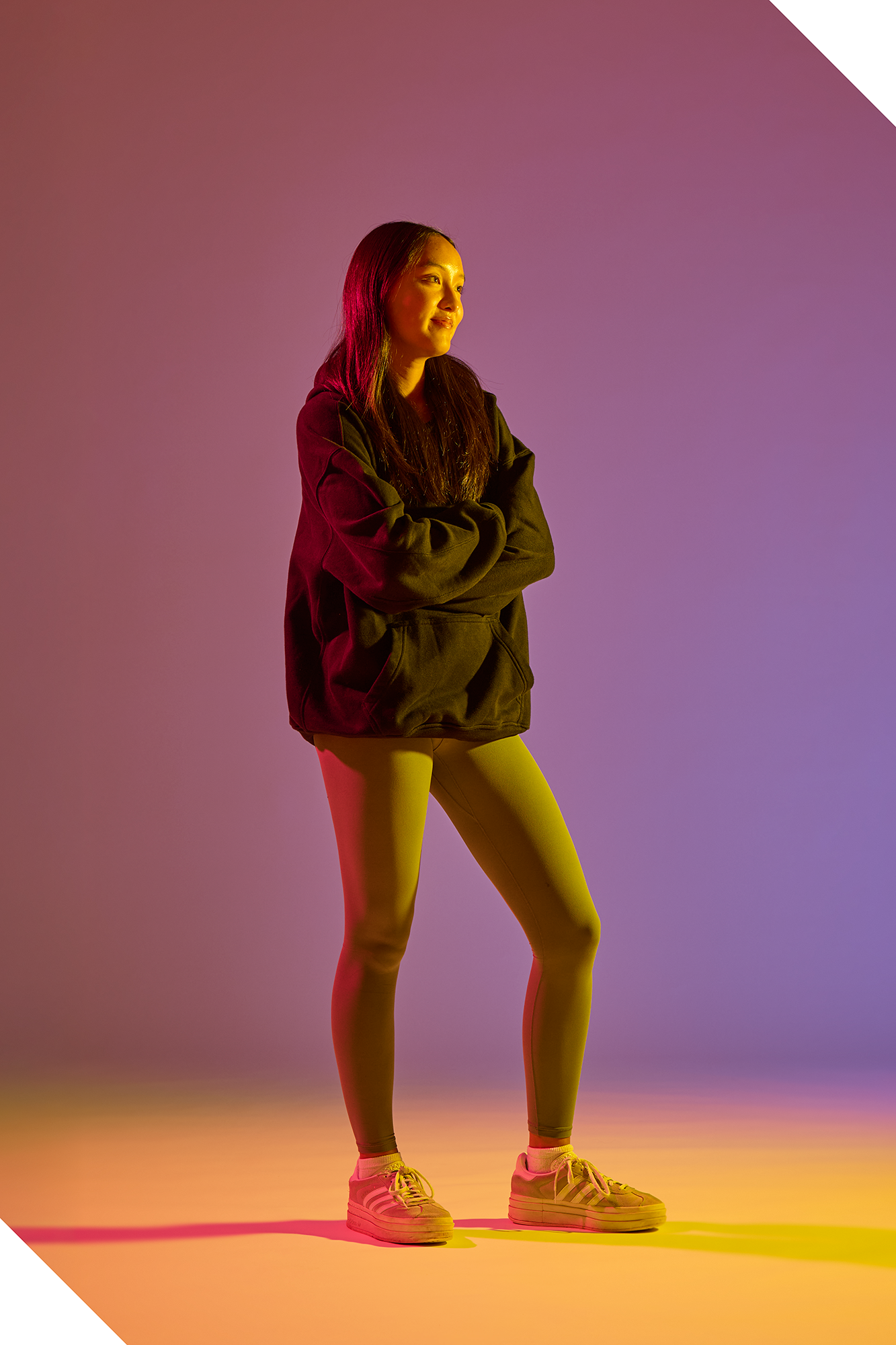 LJ Aragon poses in front of a purple and yellow background, lit by pink and yellow.