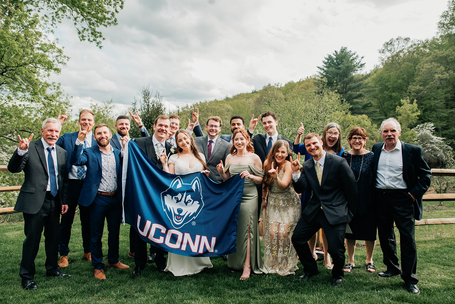 A group photo from Maya Schlesinger and Will Reid's wedding. The group holds up a UConn flag.