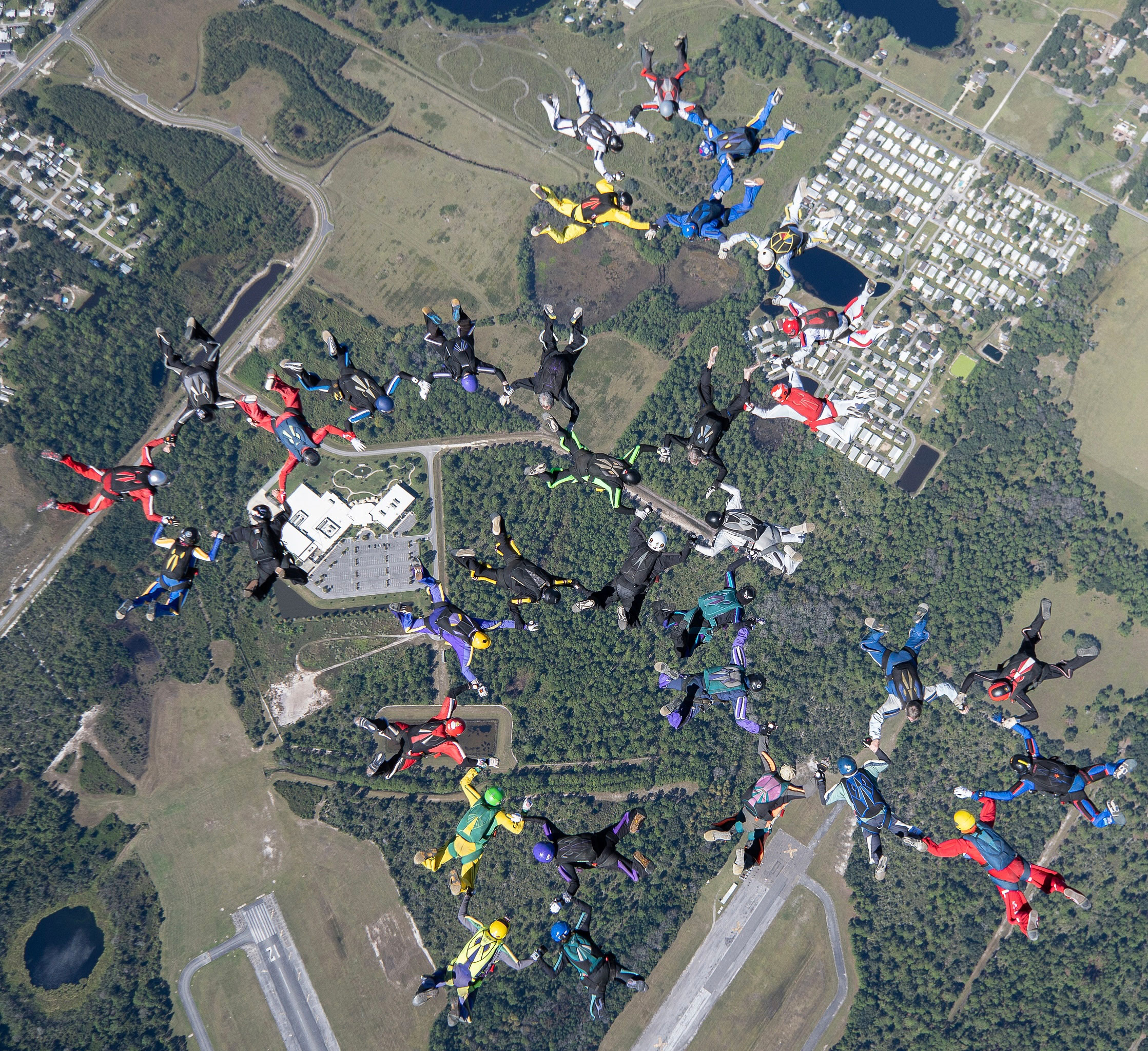 A photo of over a dozen sky divers mid-air, with Stevens to the top left in purple helmet and blue-soled sneakers.