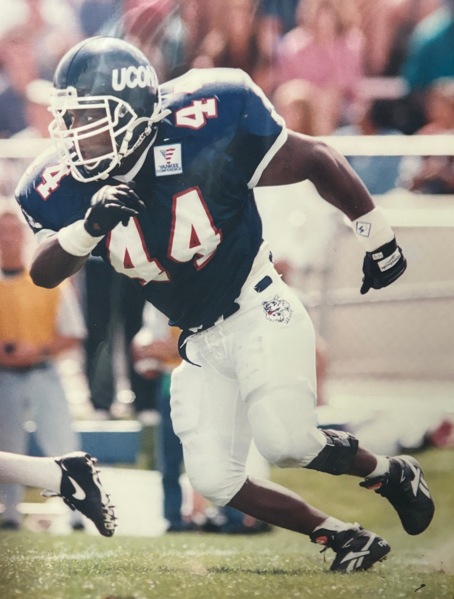 Lewis as Husky football captain during his senior year season, 1994. He is mid-running, the photo capturing him in a strong action pose.