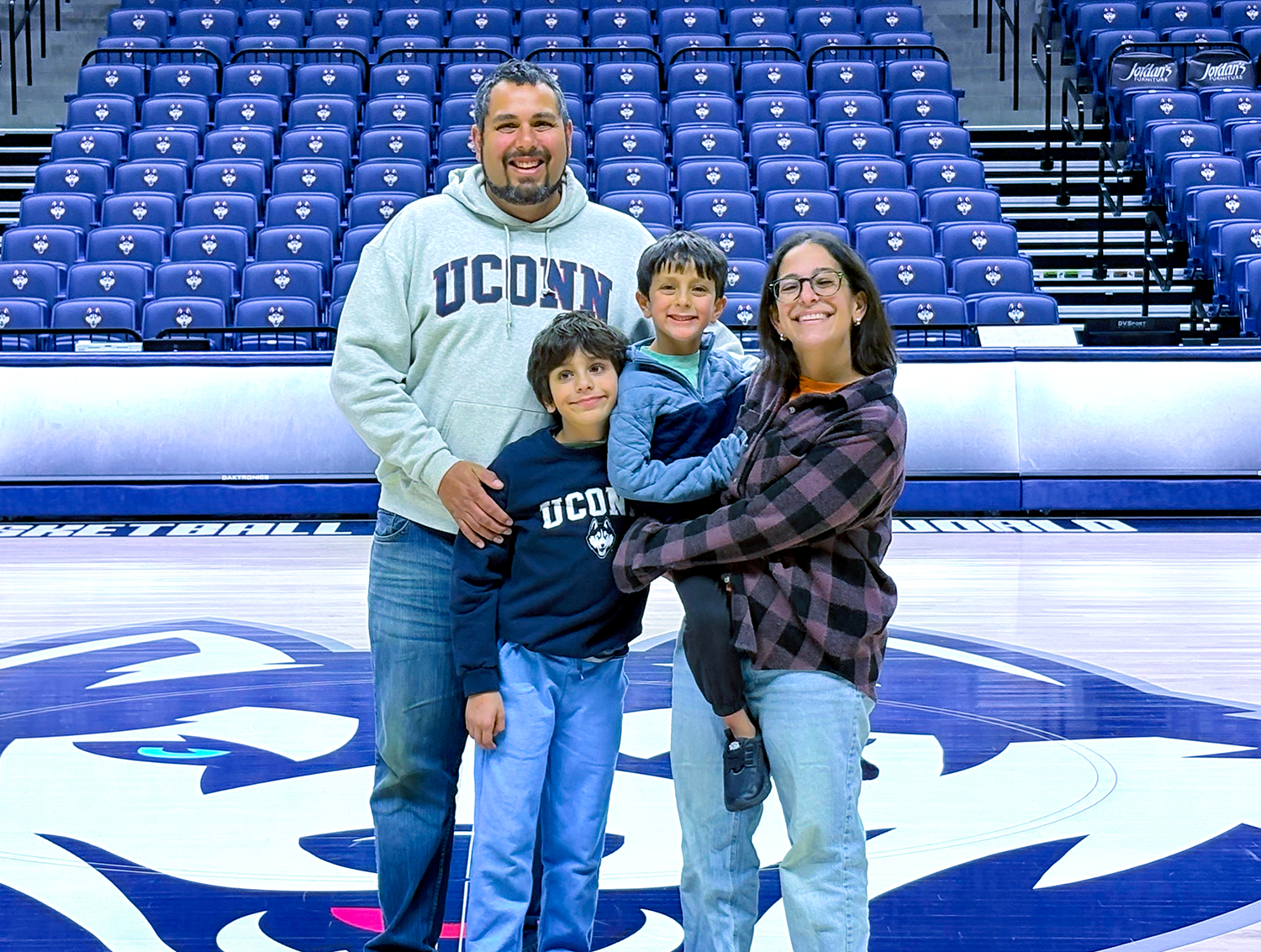 A family of four, all wearing Husky supporting outfits of blue, pose happily for the camera.