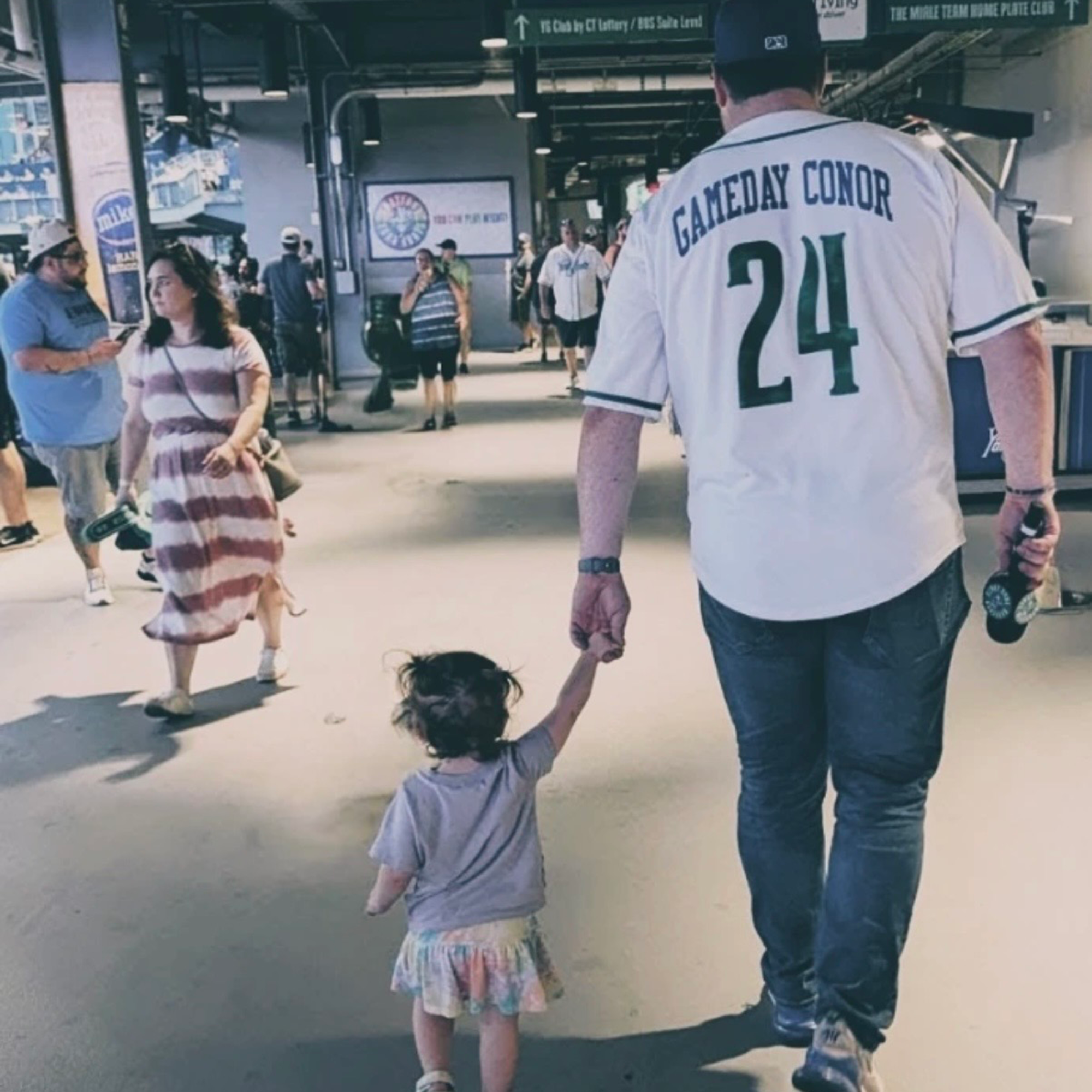 A man, Geary, and child walking together, with the man holding the child's hand. He wears a jersey with his name on it.