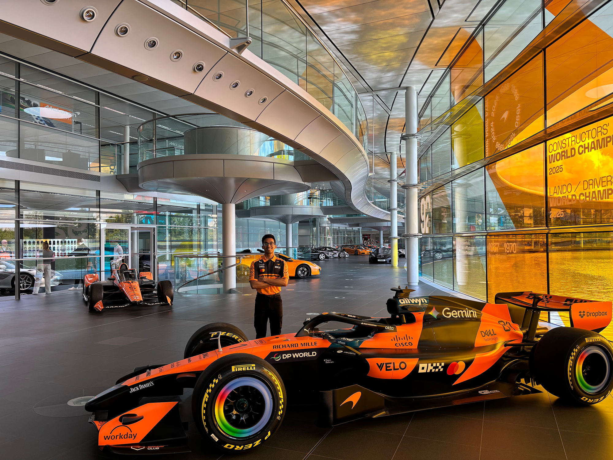 A man stands cross-armed behind an orange racing car