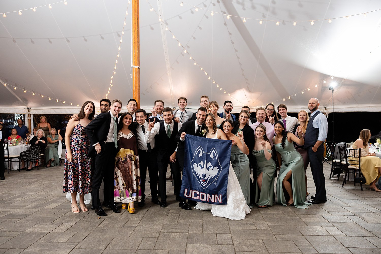 A group of people, including a bride and groom, pose for a photo in front of a UConn flag.