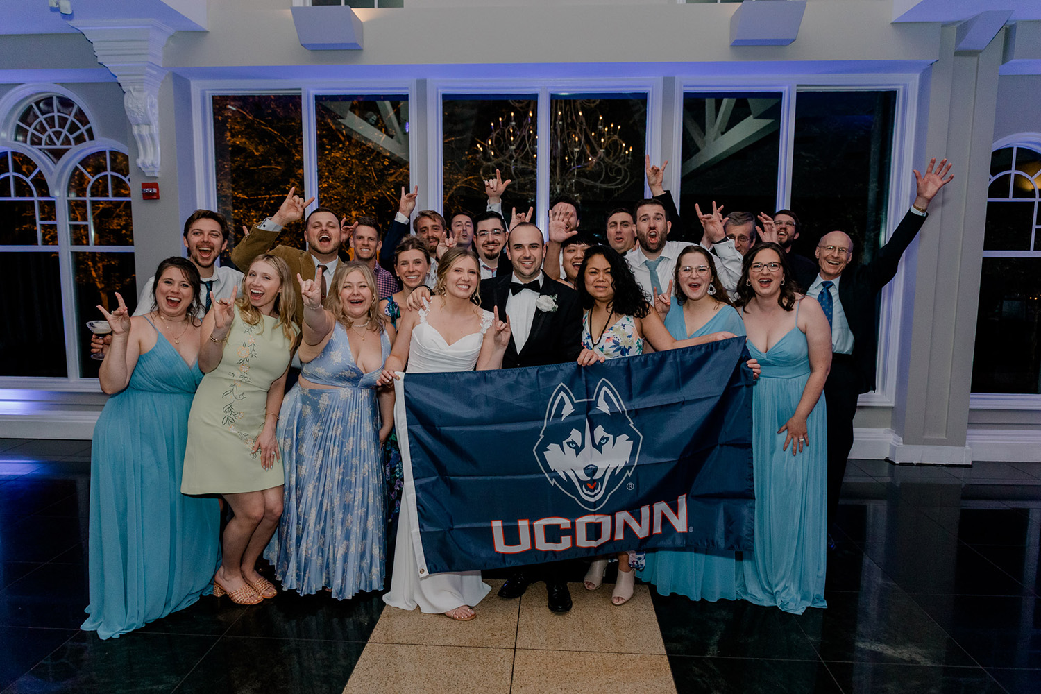 A group of people, including a bride, pose for a photo with a UConn flag.