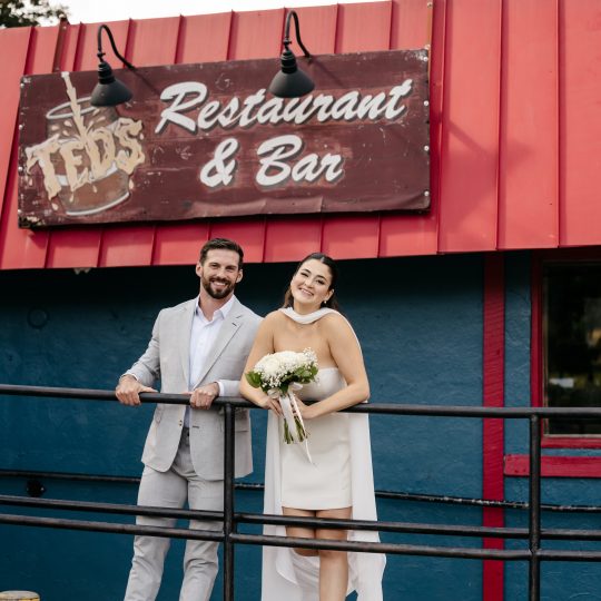 A bride and groom post in front of Ted's Restaurant & Bar