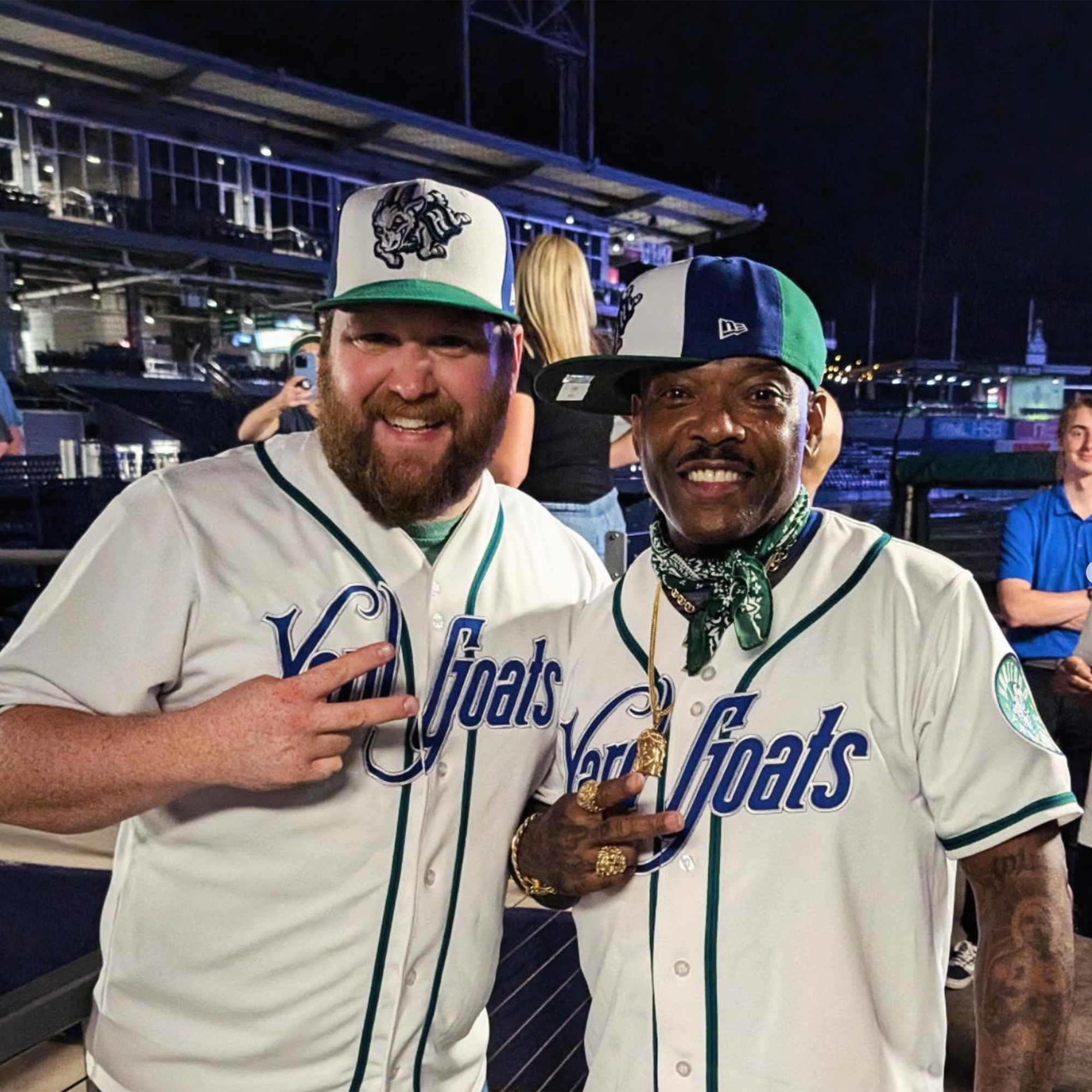 Two men, Gary and Naughty by Nature’s Treach, wearing Yard Goats baseball uniforms pose and smile for a picture. They both flash peace signs.
