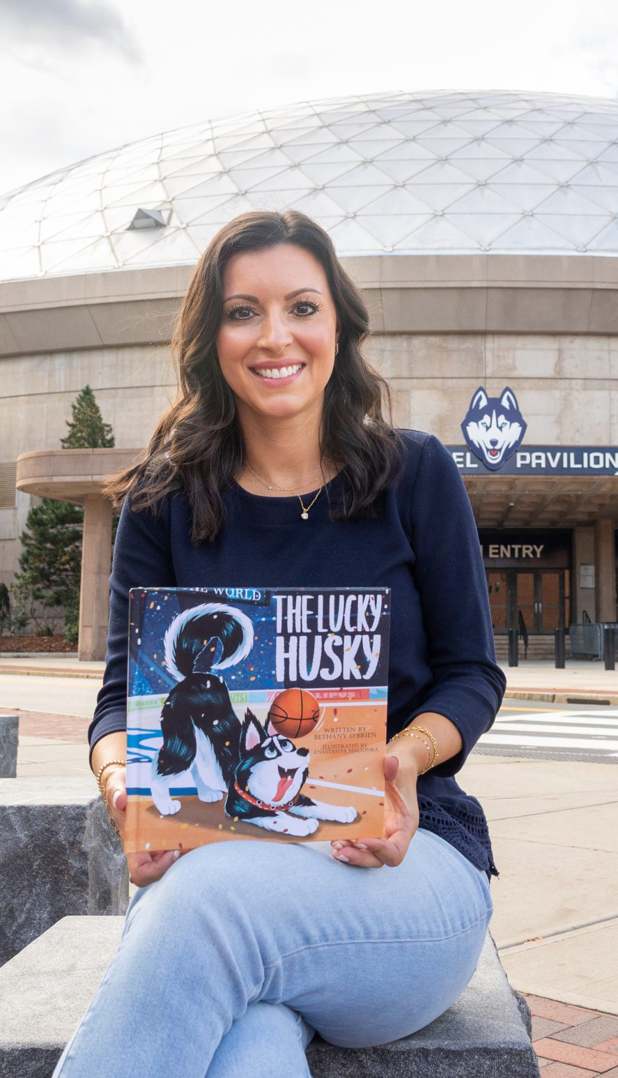 Bethany O'Brien sits at the UConn campus holding up her book.