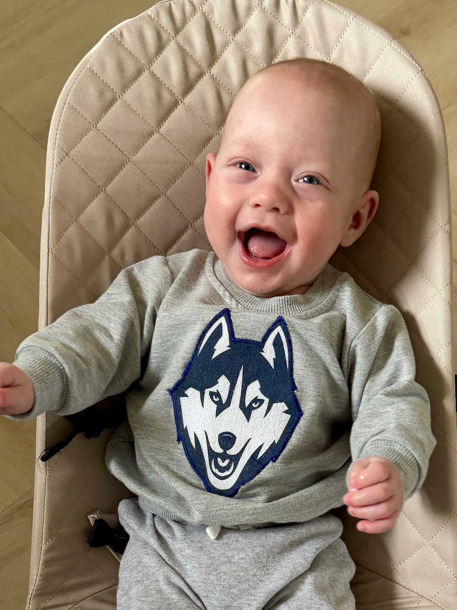 Baby boy Benson smiles cutely at the camera wearing a UConn husky sweater.