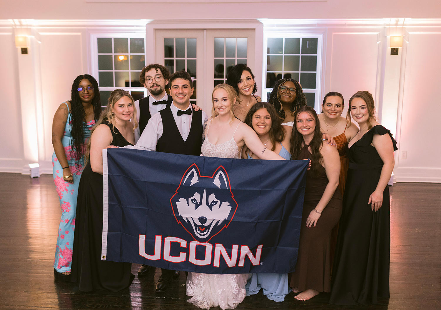 Bride and groom hold up the UConn flag in a group photo with their wedding party.