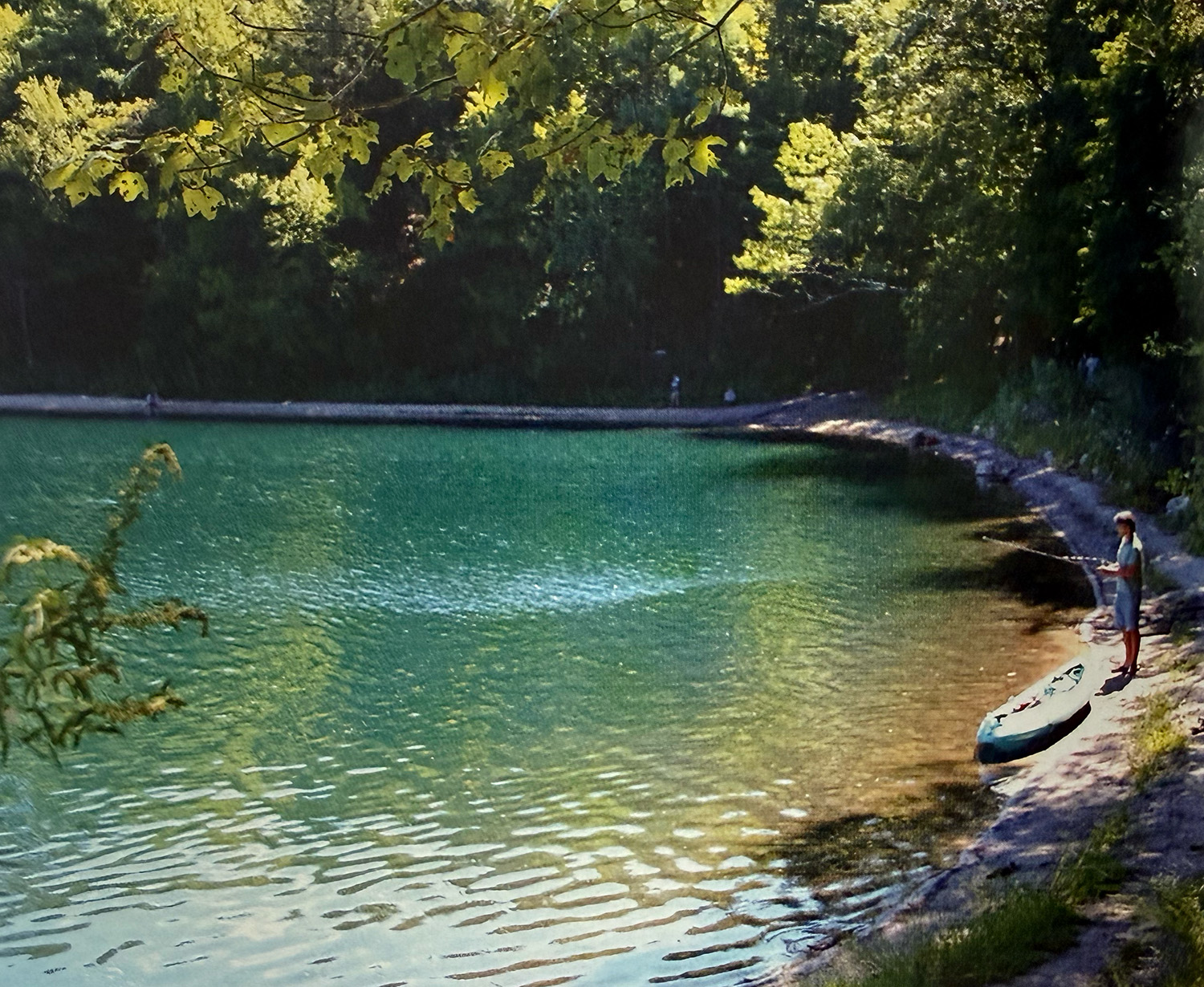 A modern photo showcasing Sandbank Cove's curved shoreline. A fisherman next to his kayak stands at the apex of the curve.