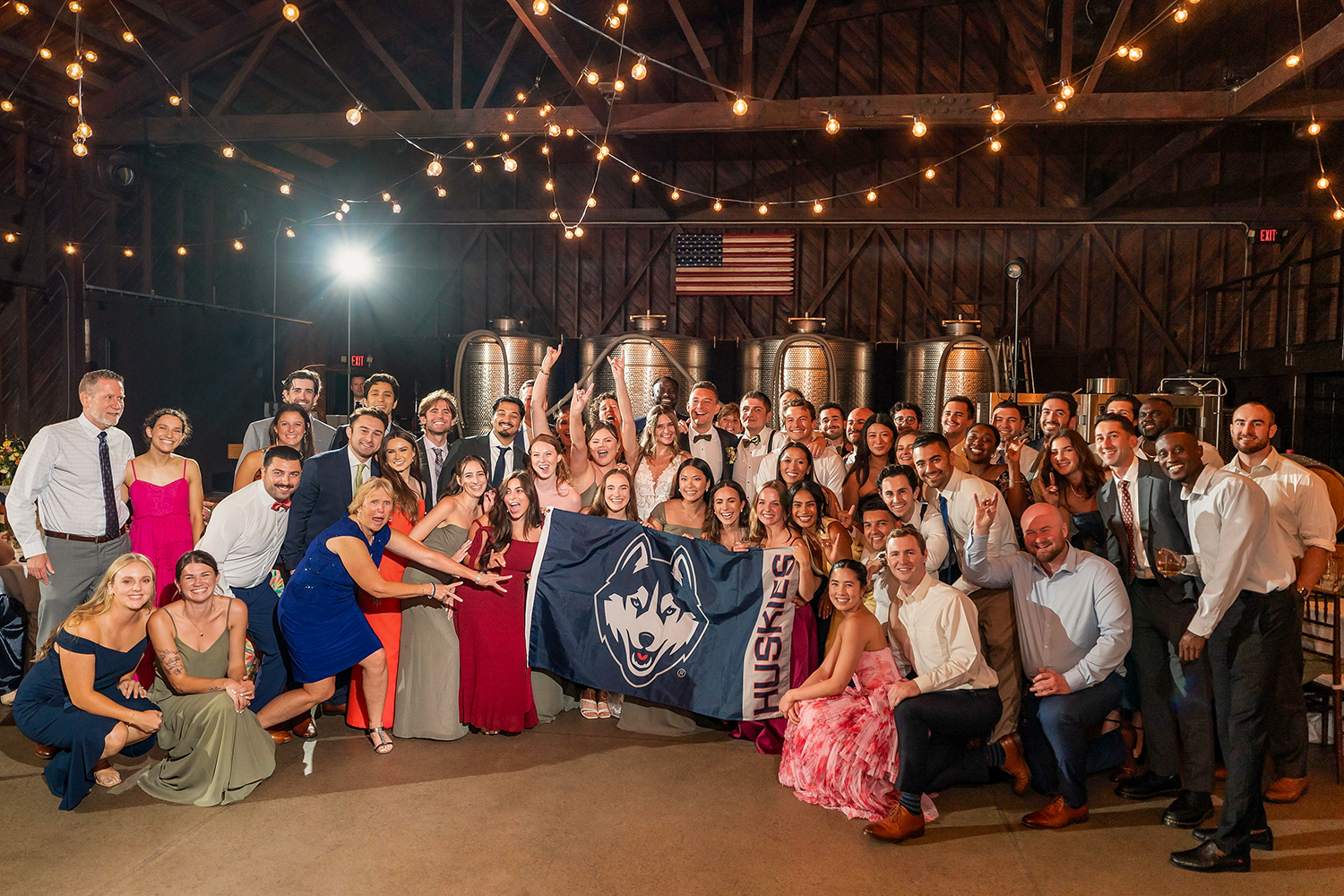 A photo of a large wedding ceremony. Bride and groom hold up a UConn flag.