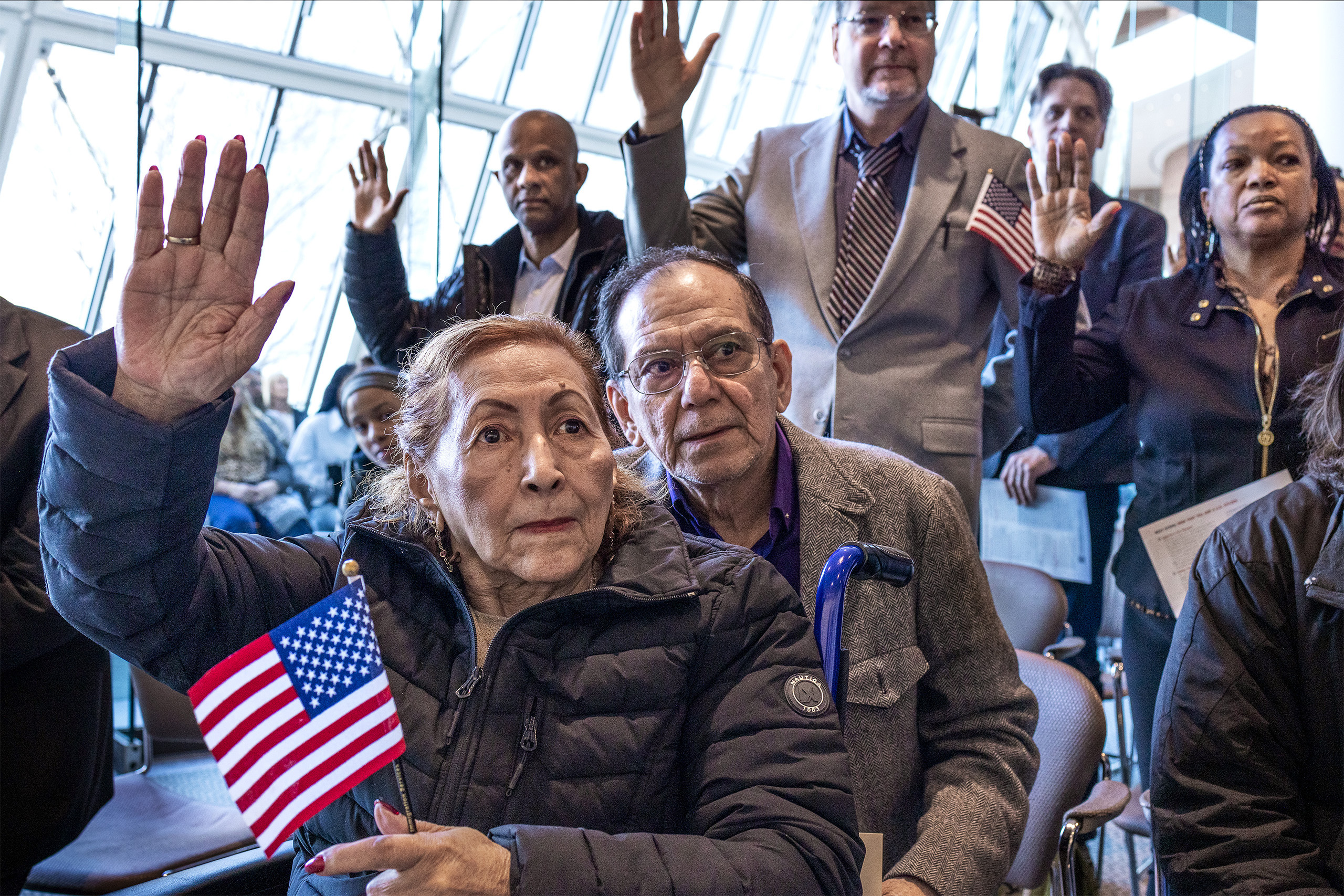 a crowd of people with raised hands and American flags at the Naturalization Ceremony, in Boston, Massachusetts