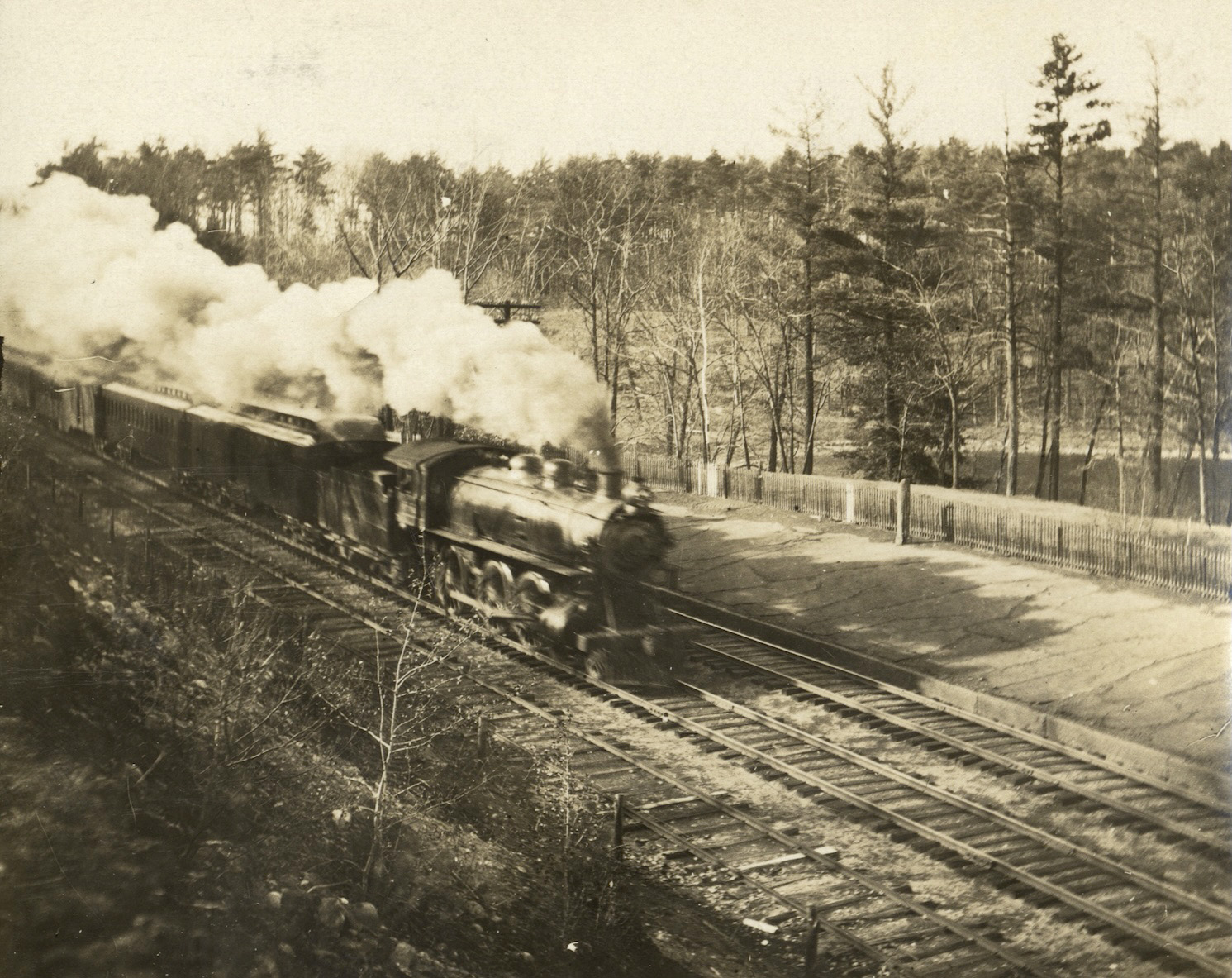 A sepia, vintage photo of a locomotive steaming away above Ice Fort Cove.