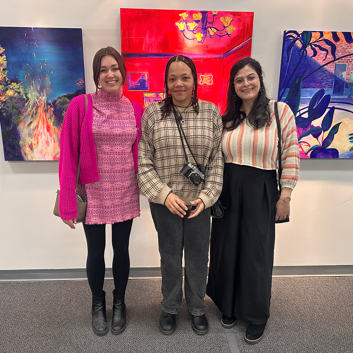Christy Corey, Jasmine Jones, and Diana Abouchacra pose together in front of a wall of art.